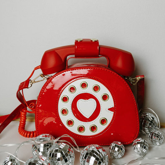 Red telephone-shaped handbag with a heart design on a light gray background